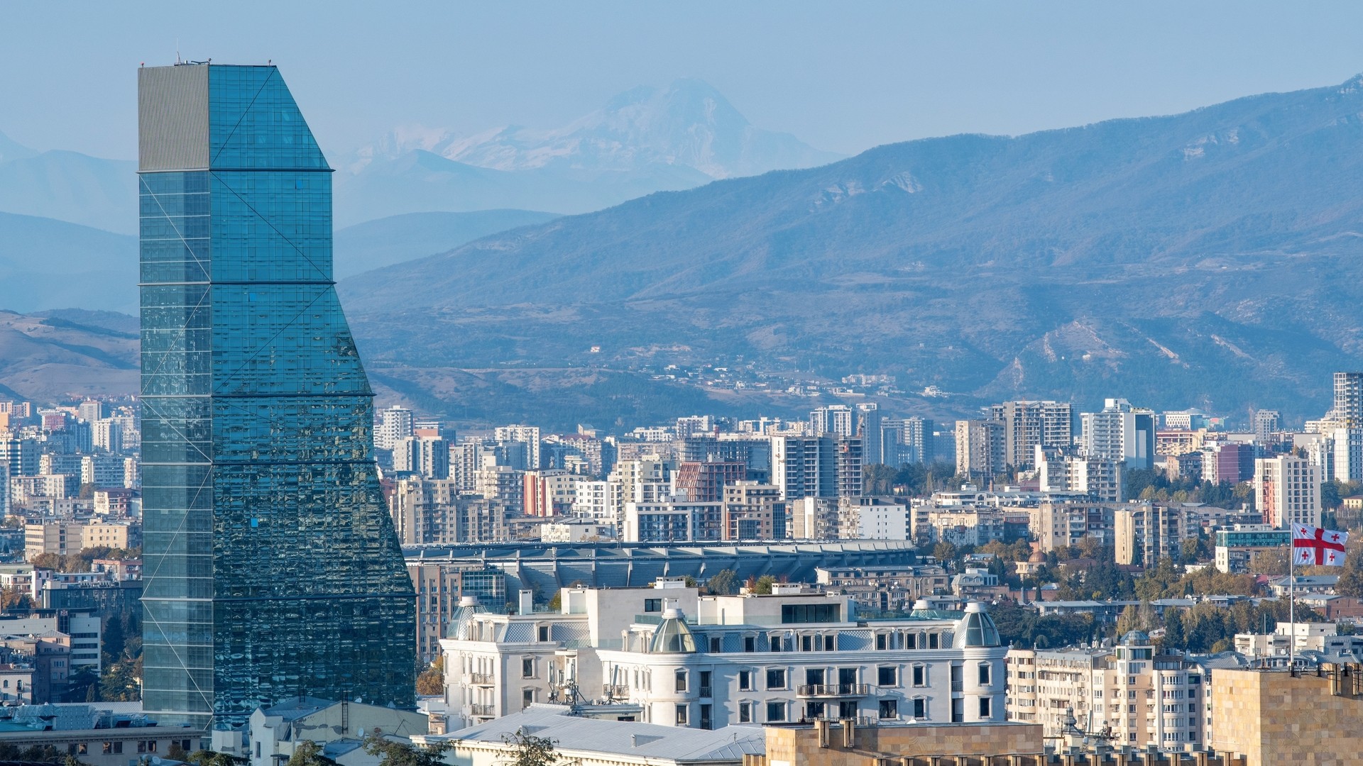 The Biltmore Tbilisi Hotel и Кавказский горный хребет в солнечный день.